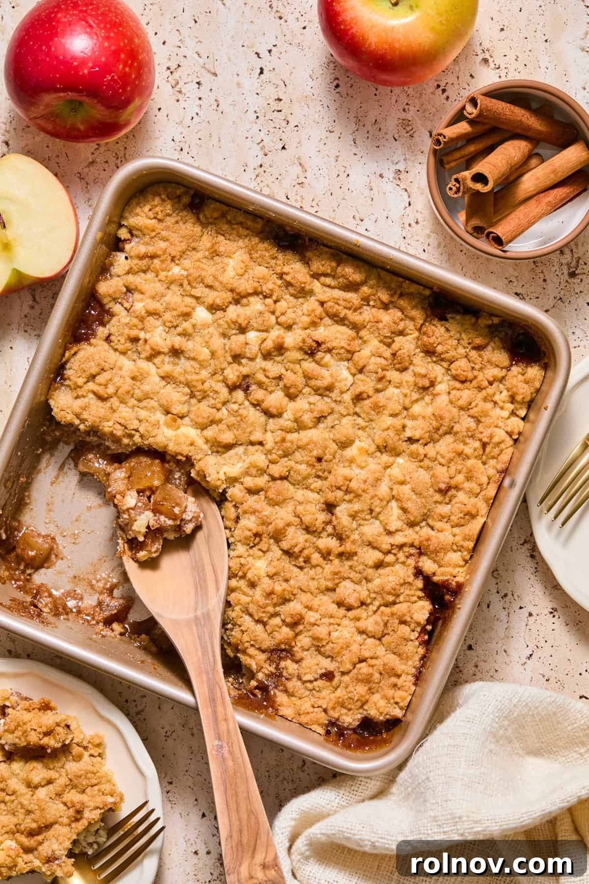 Apple cheesecake cobbler in pan with wooden spoon.