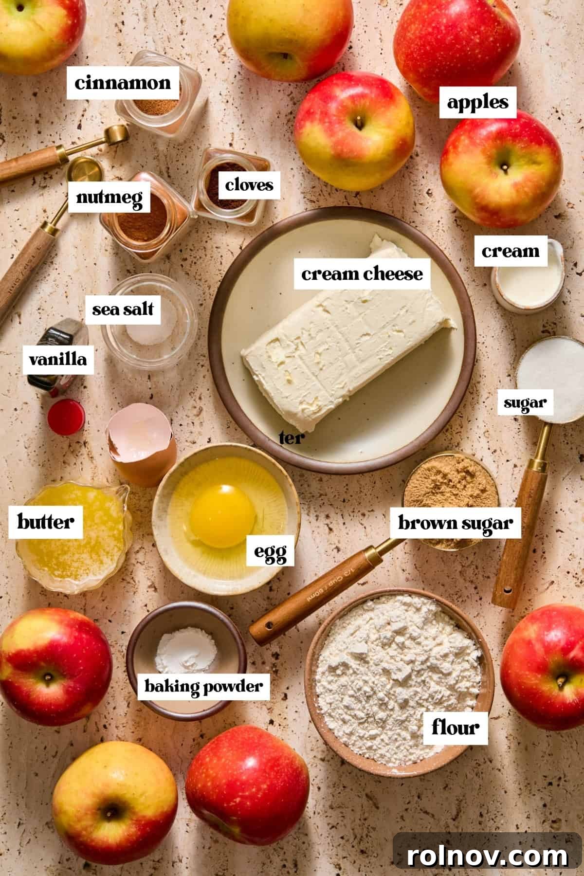 Cream cheese, apples, warm spices, egg, flour and other labeled ingredients on surface.