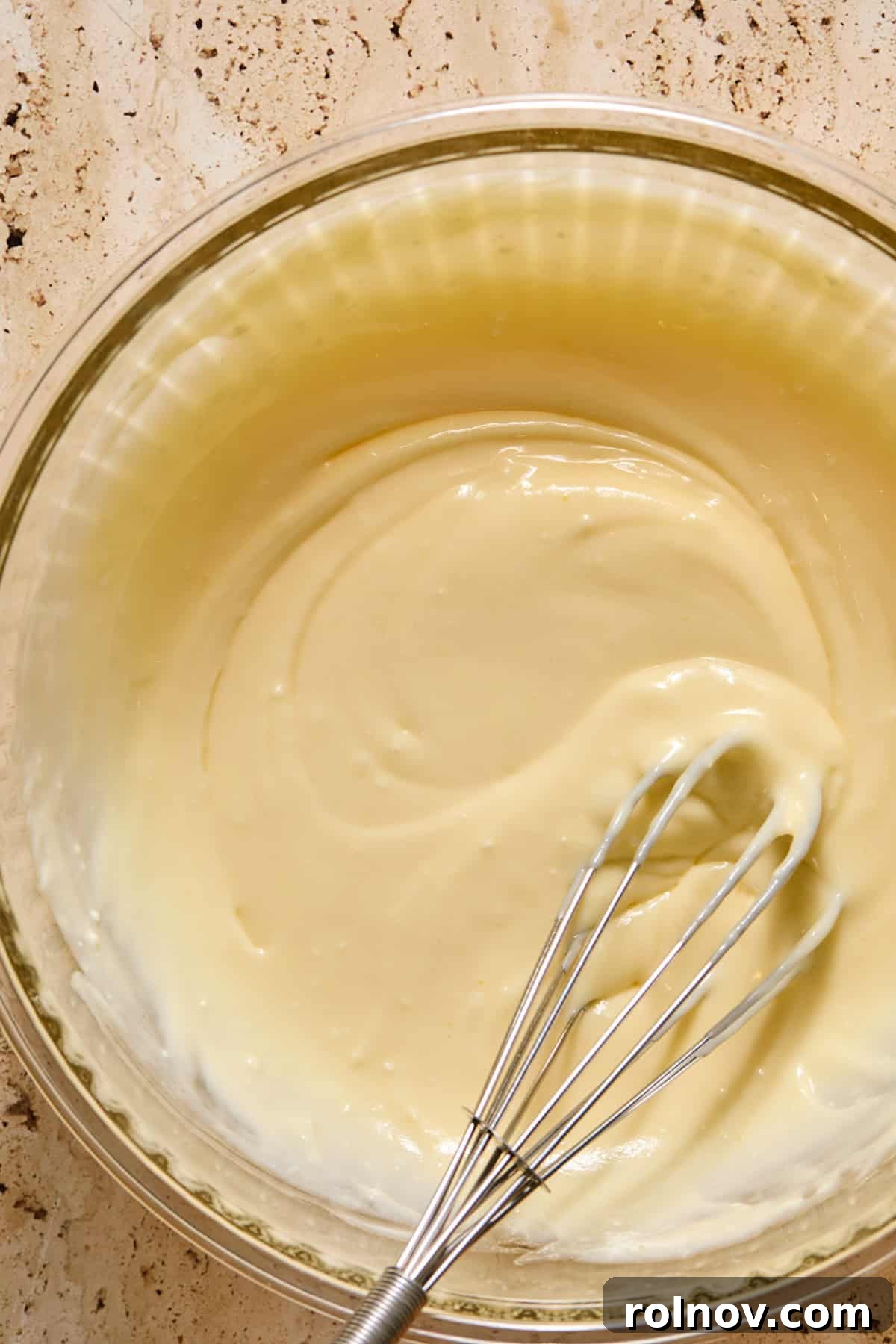 Cheesecake mixture in glass bowl with whisk.