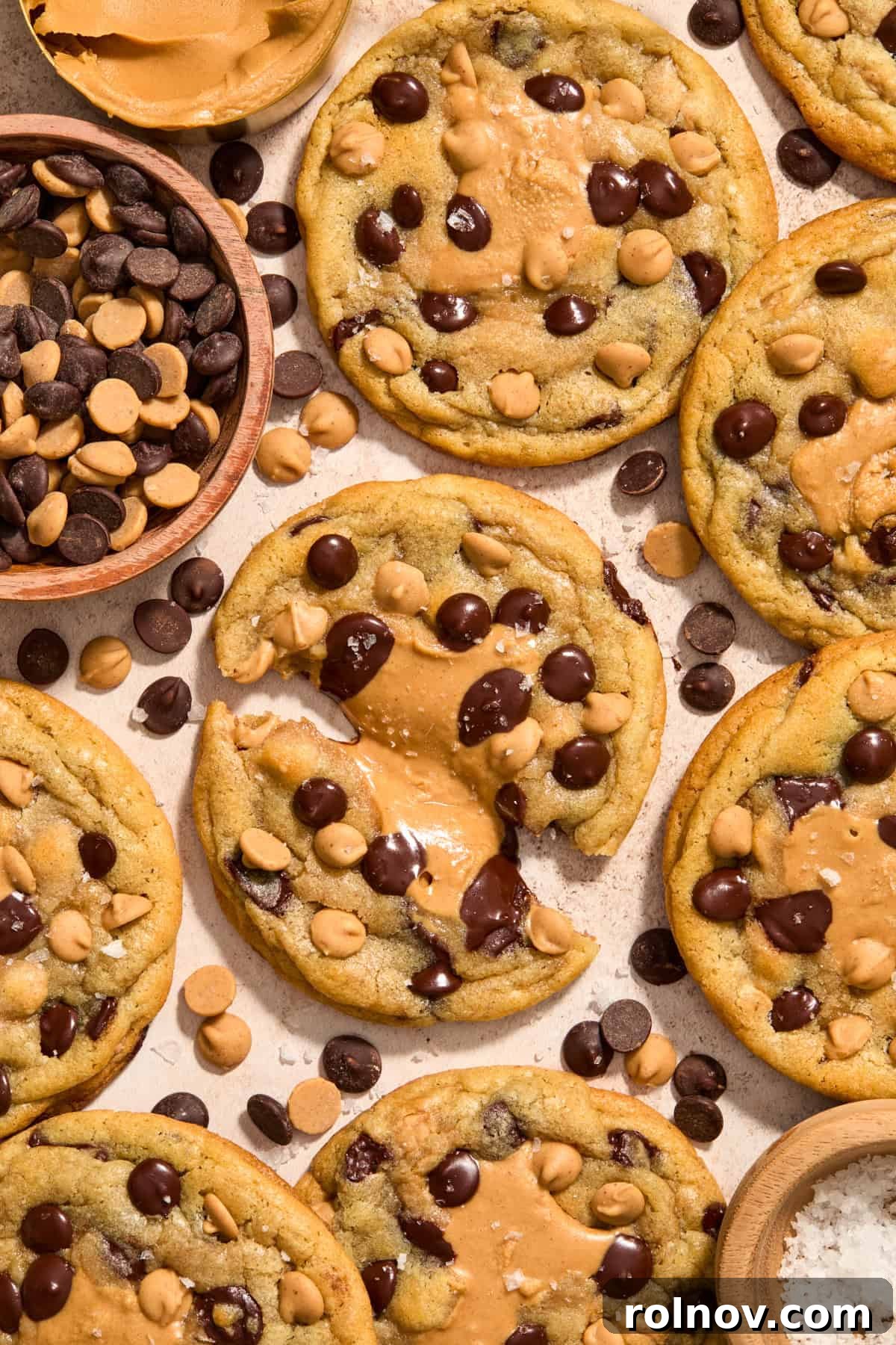 Peanut butter stuffed chocolate chip cookies on surface with one cookie pulled apart to show peanut butter center.