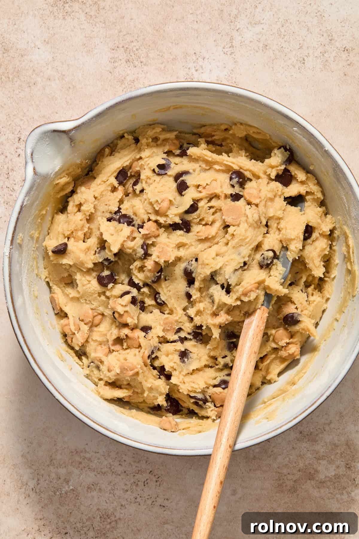 Peanut butter chips and chocolate chips mixed into cookie dough with spatula.