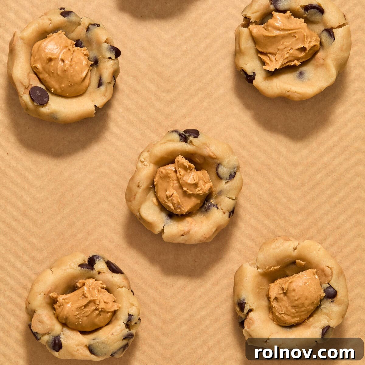 Peanut butter dollops in cookie dough balls on pan.